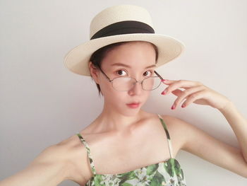 Close-up portrait of young woman wearing hat against white background