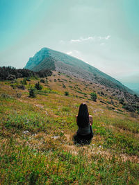 Rear view of woman sitting on mountain against sky