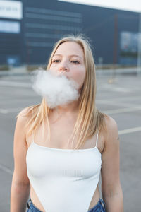 Blonde woman in city with electronic cigar vaping in white t-shirt outdoors