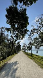 Empty road amidst trees on field against sky