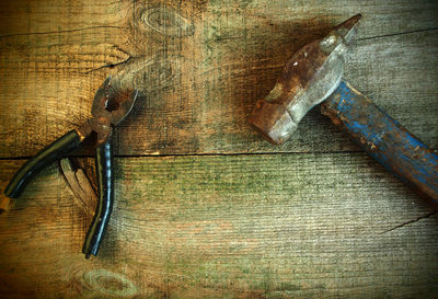 High angle view of old rusty pliers and hummer on wooden table