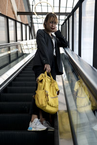 Portrait of businesswoman with backpack standing by railing on escalator