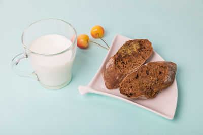 Pieces of rye bread on a white plate, next to a mug with milk on a blue background.