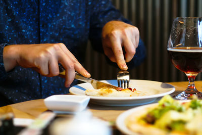 Hungry young man with knife and fork cutting and eating pizza in cafe by dinner.