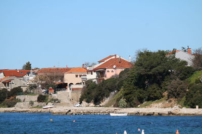 Buildings by river against clear blue sky