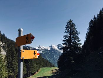 Road sign by trees against clear blue sky