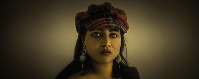 Portrait of young woman wearing hat against wall
