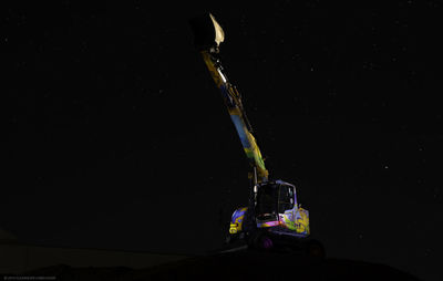 Low angle view of illuminated lighting equipment on field against sky at night