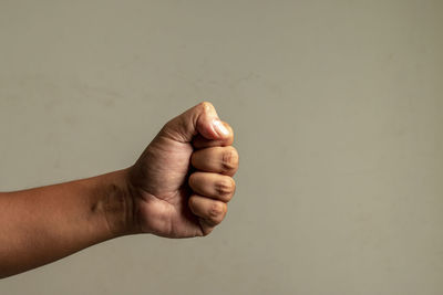 Cropped image of hand clinching fist against gray background