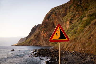 Information sign on rock by sea against clear sky