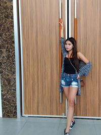 Portrait of young woman standing against door