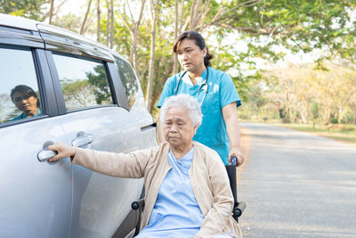 Full length of smiling young woman sitting on car