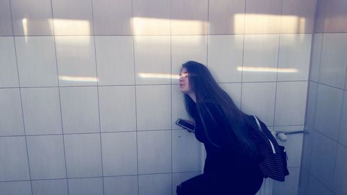Side view of woman standing against wall in bathroom
