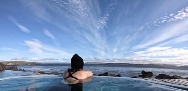 Rear view of man standing on rock by sea against sky