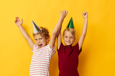 Portrait of smiling girl with arms raised standing against yellow background