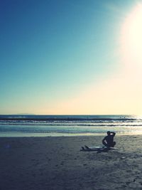 Silhouette man sitting on beach against clear sky