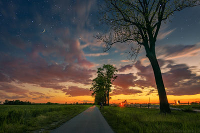 Road amidst field against sky during sunset