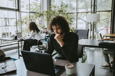 Male entrepreneur contemplating while working on laptop in coworking office