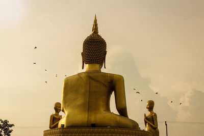 Low angle view of golden buddha statue against sky on sunny day