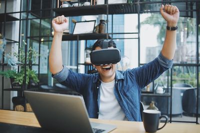 Smiling man gesturing while using virtual reality simulator at cafe