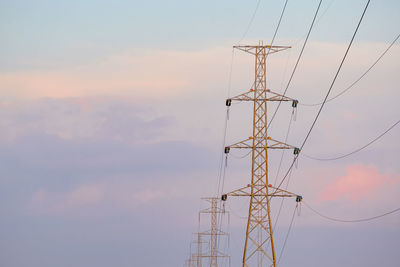 Low angle view of electricity pylon against sky during sunset