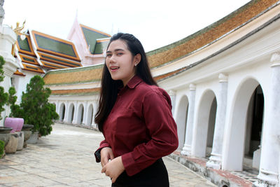 Portrait of smiling young woman standing against built structure