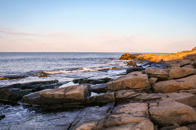 Rocks on sea shore against sky during sunset