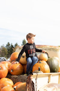 Full length of boy sitting by pumpkins against sky