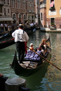 People on gondola in canal along buildings