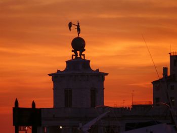 Statue in city against orange sky