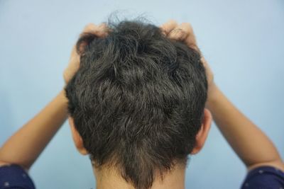 Rear view of boy with hands in hair at home