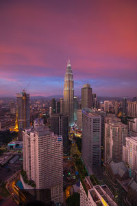 Petronas towers and buildings in city against cloudy sky during sunset