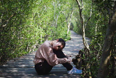 Side view of young man sitting on land in forest