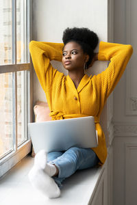 Young woman with laptop sitting by window at home