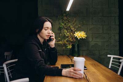 Young woman using mobile phone while sitting on table