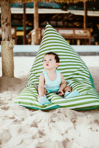 Cute boy looking away while sitting at beach