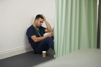 Worried male nurse with head in hand sitting by wall in medical room