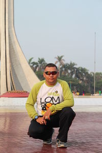 Portrait of man wearing sunglasses while crouching on footpath