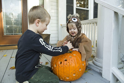 Two boys play with jack o lantern on front porch while dressed up