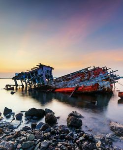 Abandoned boat sinking in sea against sky during sunset