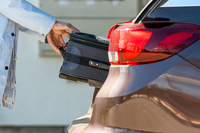 Cropped hand of woman removing suitcase from car trunk