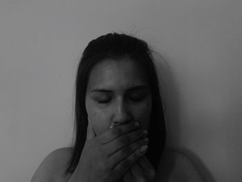 Young woman with eyes closed covering mouth against wall