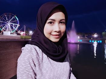 Portrait of smiling young woman against illuminated sky at night