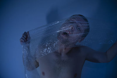 Shirtless man pulling plastic on his face