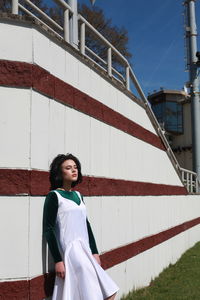 Young woman with eyes closed standing by wall during sunny day