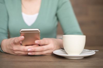 Close-up of woman holding coffee cup on table