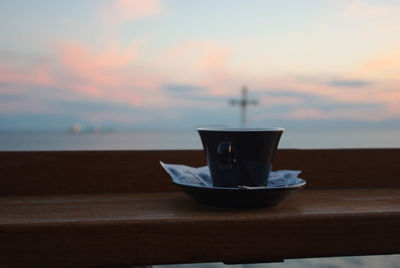 Close-up of coffee cup on table against sky during sunset