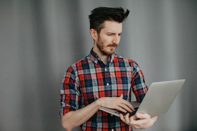 Handsome young man in a plaid shirt by a grey background with laptop. high quality photo