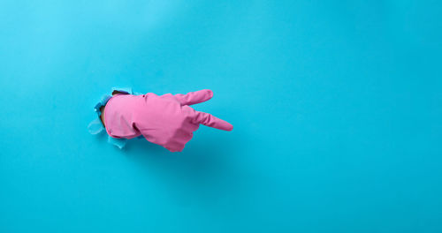 Hand in a pink latex glove points a finger on a blue background. place for inscription 