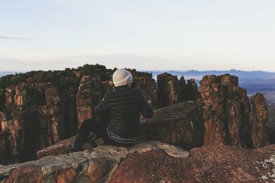 Rear view of woman sitting on cliff against sky